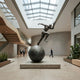 Giant Sculptures' 330cm Monumental Contemporary Male Runner Bronze Sculpture balanced on a sphere in a skylit atrium, with figures walking past for scale.