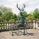 Giant Sculptures Monumental Contemporary Seated Stag Bronze Sculpture 250cm with verdigris patina, seated upright on a metal stand on a stone terrace.
