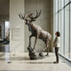 Monumental Rearing Bull Moose Bronze Sculpture by Giant Sculptures with dark brown patina on a rocky base, shown at 300cm beside a woman in a museum interior.