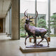 Monumental Traditional Striding Stag Bronze Sculpture by Giant Sculptures displayed in a concrete gallery beside floor-to-ceiling windows overlooking a Japanese garden.