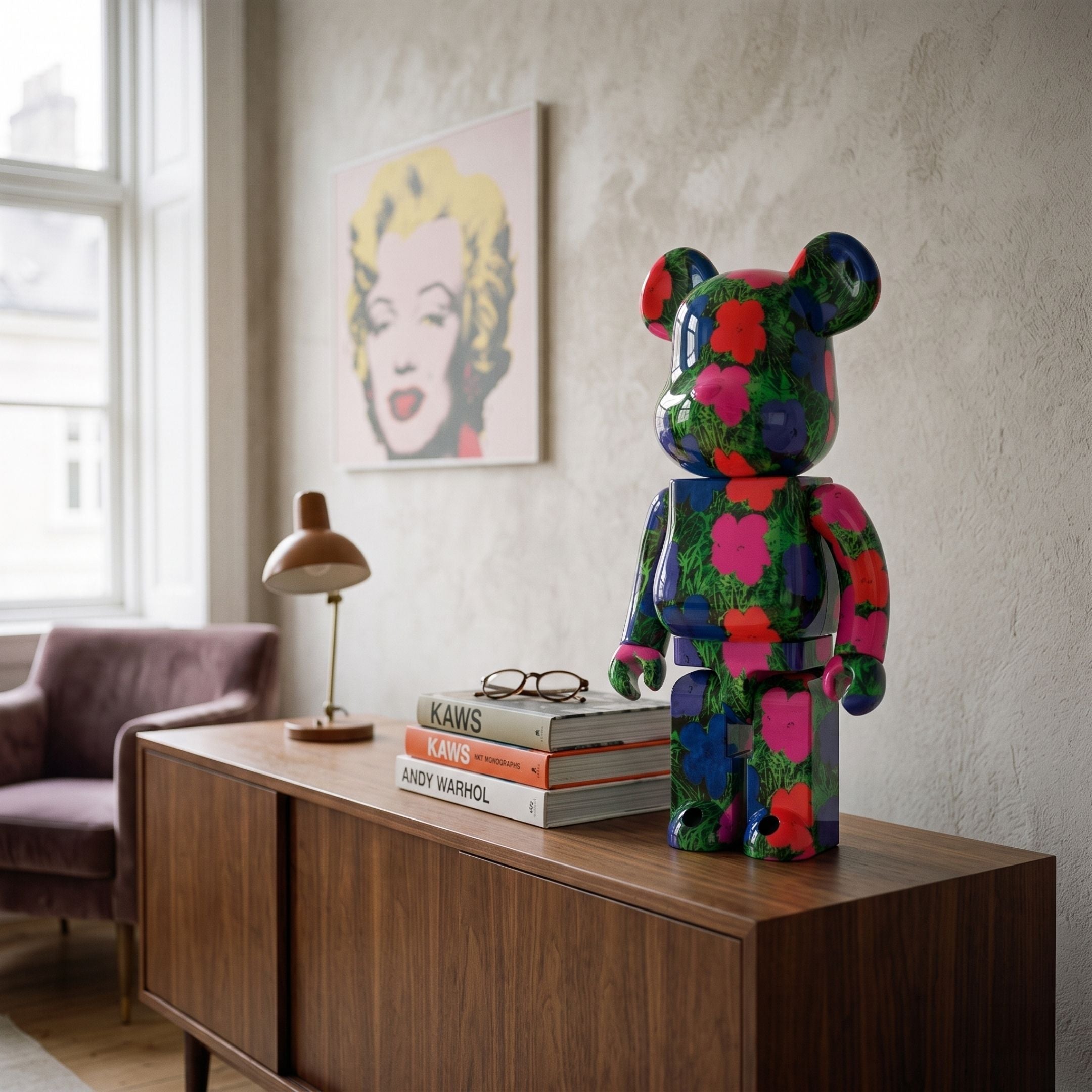 Neon Meadow Bear Sculpture - 70cm in gloss resin with pink, red, blue, and green floral pattern, displayed on a wooden sideboard near art books and a wall print.