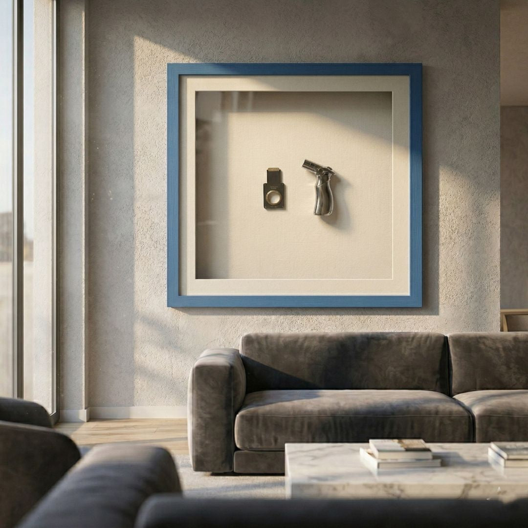 Valet Noir Cigar Cutter & Torch Blue Framed Wall Art by Giant Sculptures displayed in a modern living room above a grey velvet sofa, featuring a chrome torch and metal cigar cutter mounted on a white background within a blue wood frame.