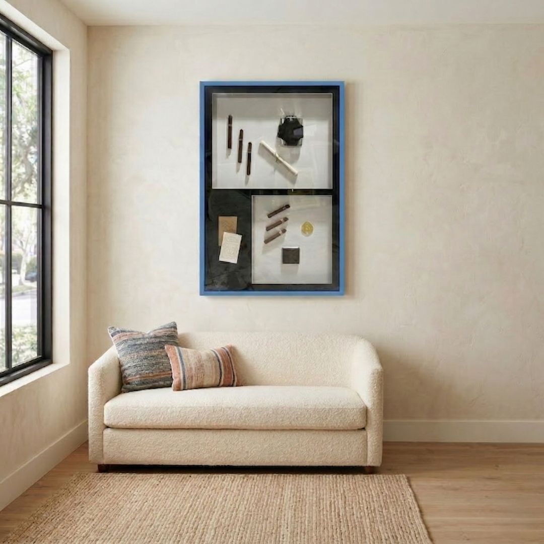 Valet Noir Gentleman Cigar Gallery Box Framed Wall Art by Giant Sculptures in a blue wood frame, displayed above a cream sofa in a neutral living room setting.