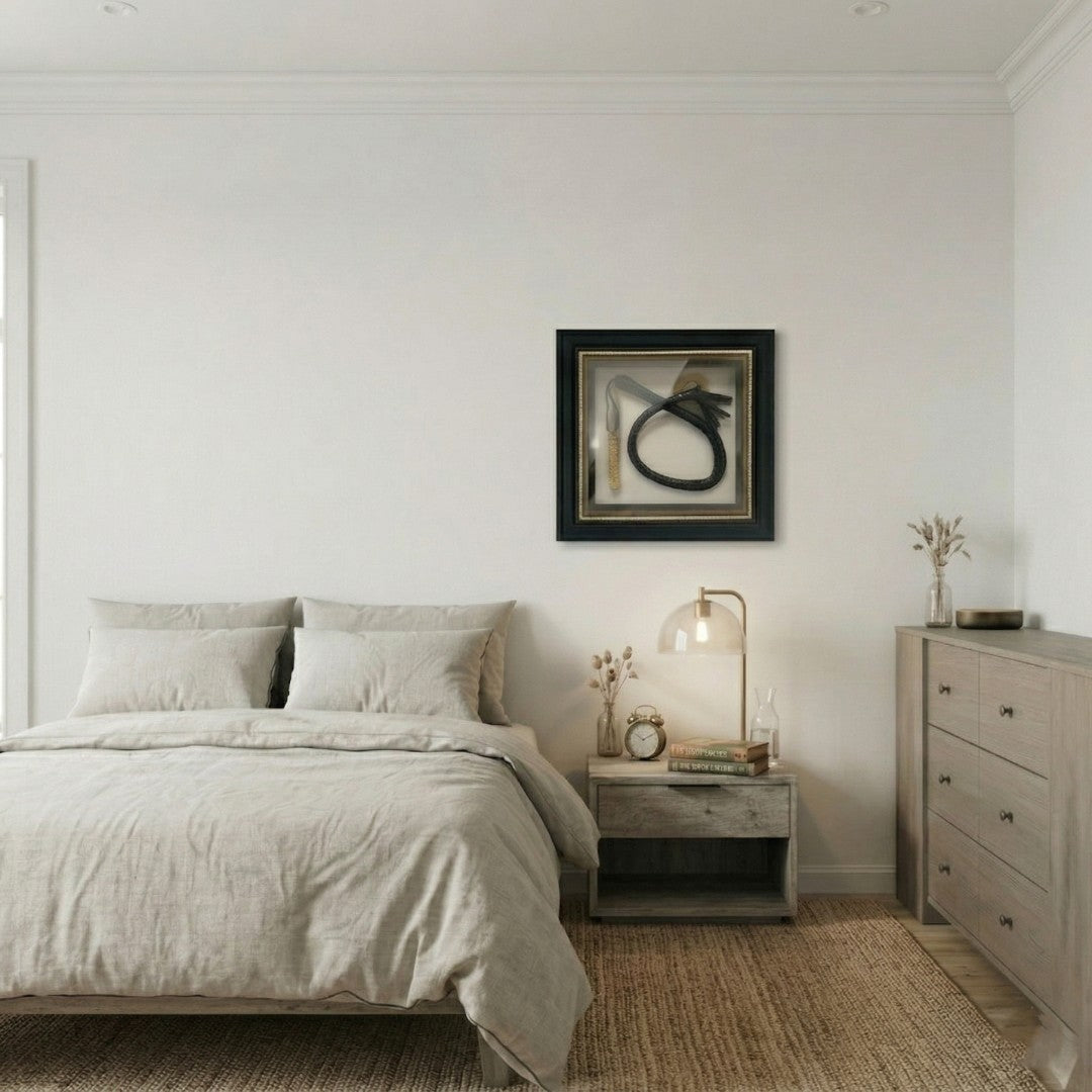CurioVault Braided Leather Loop & Medallion Framed Wall Art displayed in a neutral bedroom above a linen-covered bed, beside a wooden nightstand and light oak dresser.