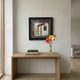 CurioVault Cigar & Sheet Music Framed Wall Art by Giant Sculptures displayed in a hallway above a wooden console table with books and colorful gerbera daisies.