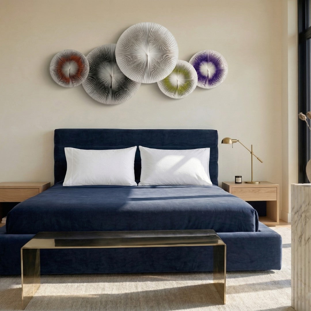 Centria I Multicolour Disc 5-Panel 3D Leather Wall Art by Giant Sculptures displayed above a navy velvet bed, showing five overlapping radial discs in orange, black, grey, yellow, and purple tones against a warm beige wall.
