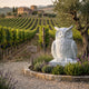 Perched Owl White Marble Statue - 150cm by Giant Sculptures on a plinth amid lavender in a vineyard garden, olive tree and rows of vines behind.