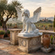 Winged Dog Marble Memorial Statue - 120cm, seated with wings spread and head raised, on a carved pedestal amid an Italian terrace and countryside view.