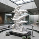 Five Dolphins on a Wave Column Marble Statue - 180cm in white, grey-veined marble on a black plinth, displayed in a modern glass-walled courtyard.