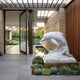Leaping Dolphin White Marble Garden Statue - 120cm on a stepped plinth beside a reflecting pool, set against a stone wall at a modern home's entrance.