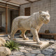 Walking Leopard Beige Marble Statue - 150cm, shown outdoors on a stone platform amid a pebbled courtyard, with rosette spots detailed across its cream-toned coat.