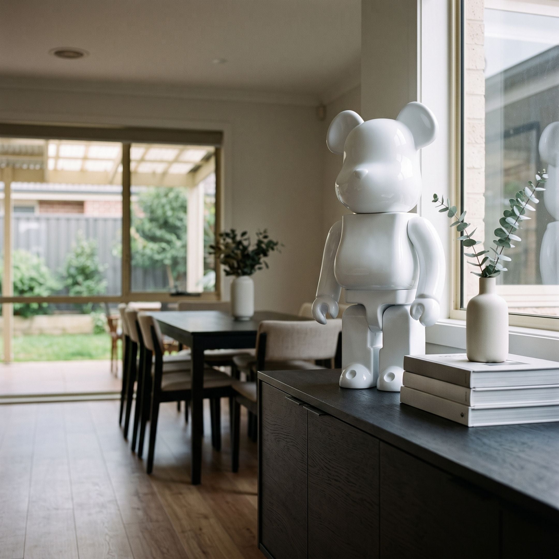 Pure White Bear Sculpture - 70cm, glossy resin bear on a dark sideboard in a dining room, near vases, books, and a wooden table.
