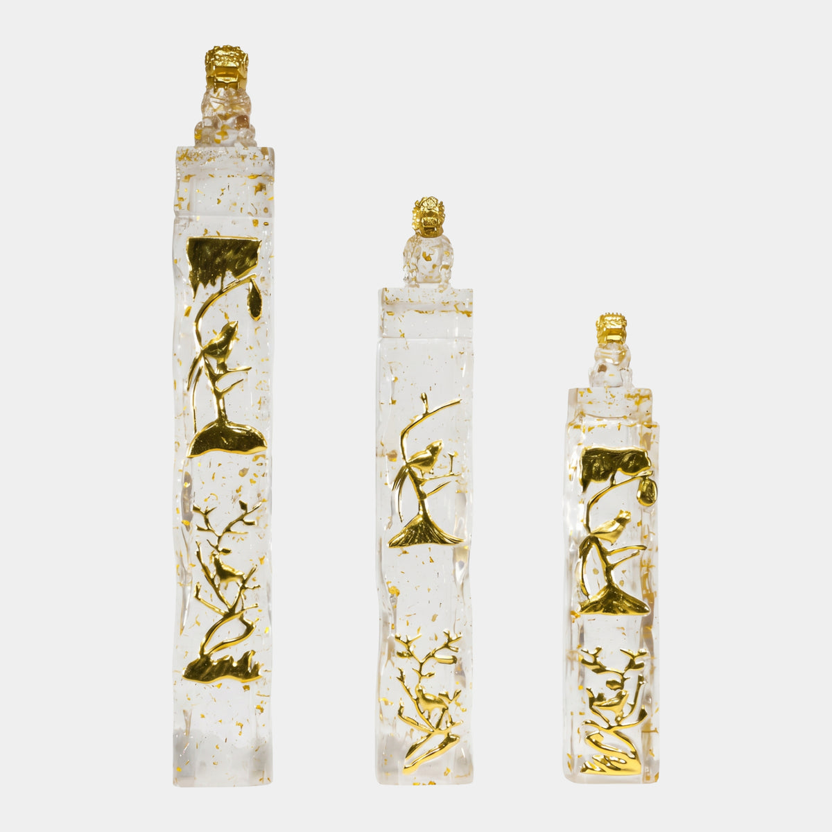 Clear Gold-Flecked Column with Bird Relief sculptures in three heights (94/117/148cm) by Giant Sculptures, each clear resin shaft with gold flecks, gilded bird and branch motifs, and a gold-headed guardian lion finial, shown on a plain white background.