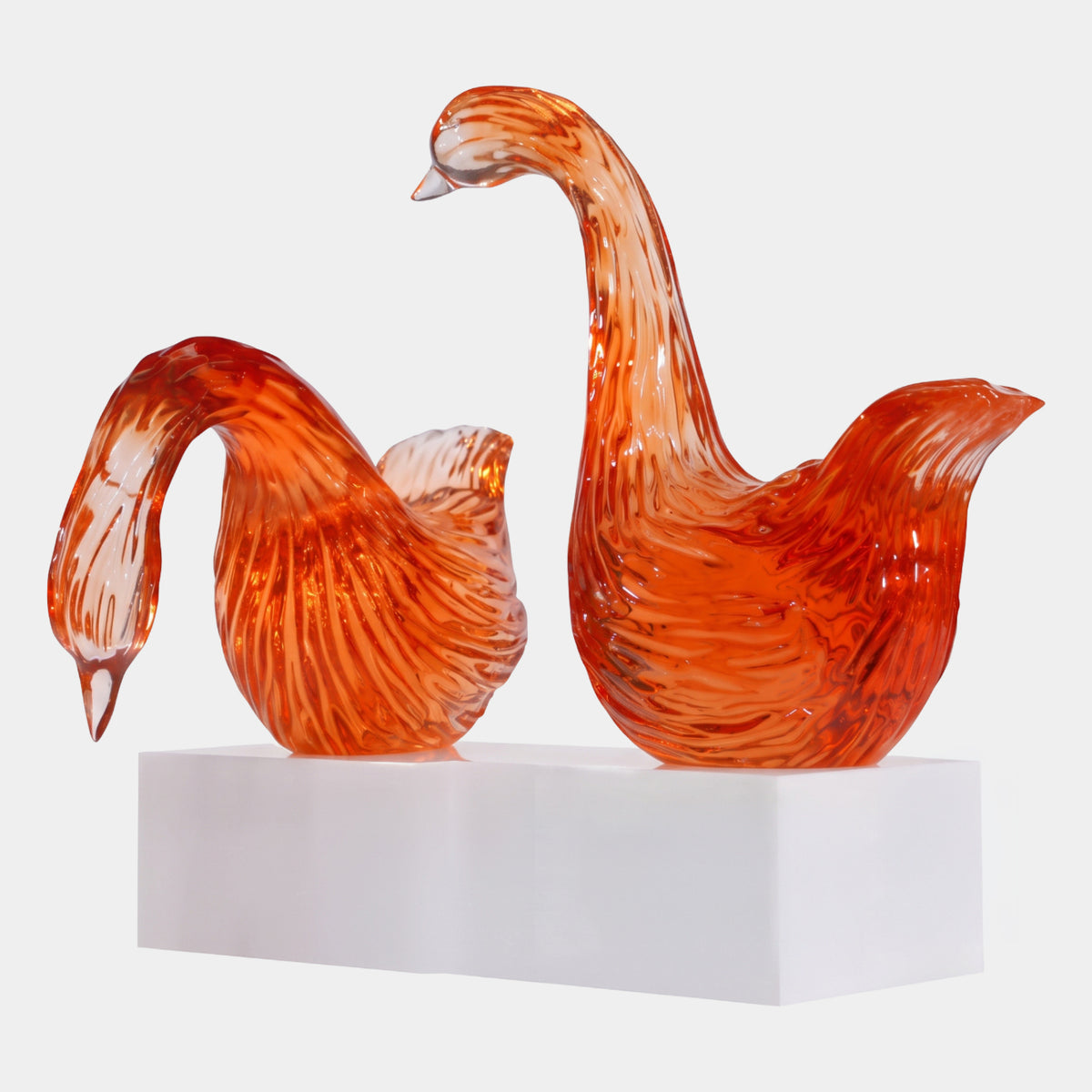 Red Feather-Cut Swan Pair on Lit Bases, 52cm, resin swans in translucent red with combed feather texture, one neck raised and one lowered, on a white acrylic base against a plain light background.