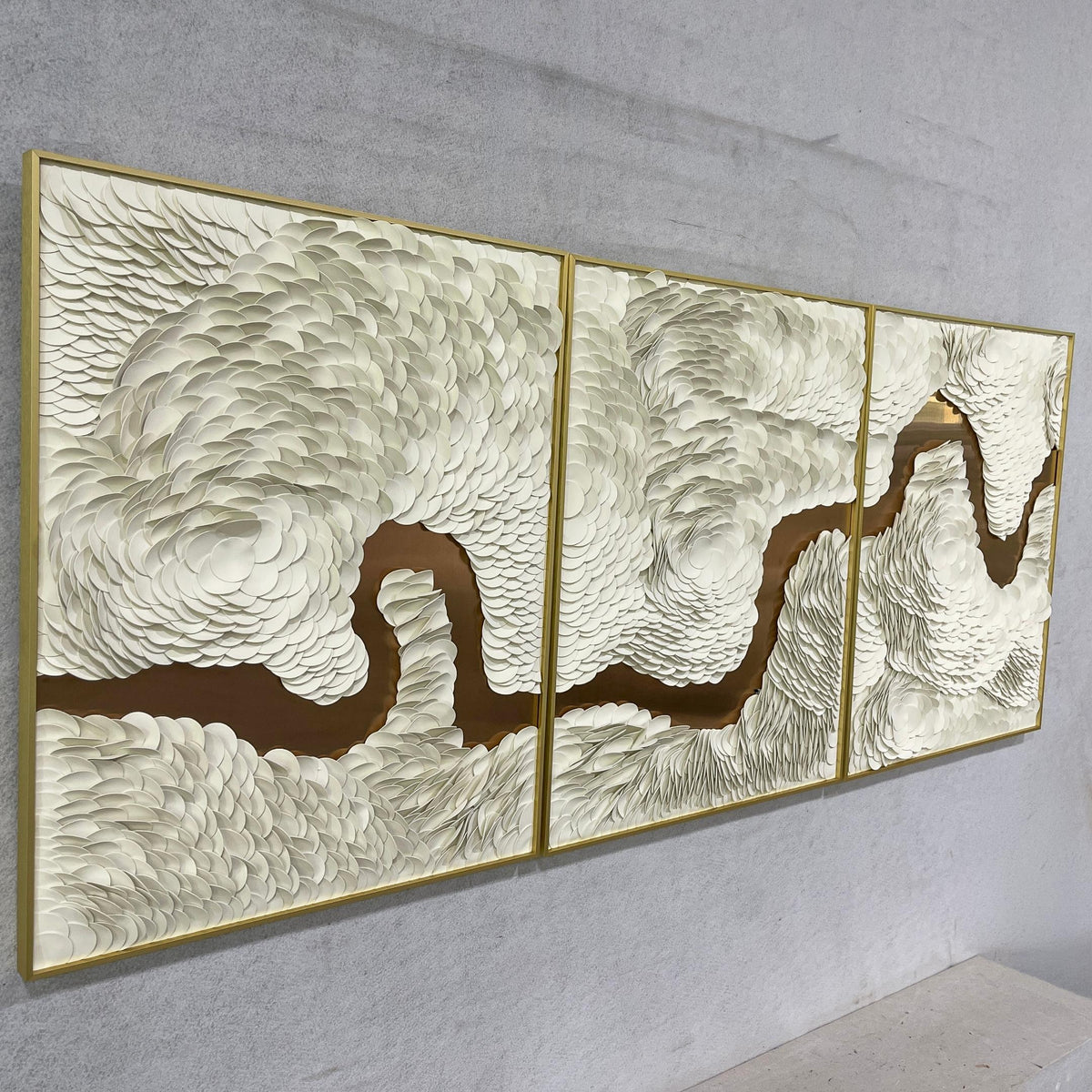 Riverine Flow Pearl White Textured Triptych Wall Art by Giant Sculptures, three gold-framed panels with sculpted white texture over a bronze flowing river motif, mounted on a light grey wall.