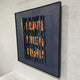 Rivura Navy Layered Sandstone Texture 3D Wall Art in a black frame, showing torn navy strips revealing orange layers, shown at an angle against a light grey wall.