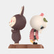The Giant Sculptures Spooky Buddies Silent Feud Labubu Sculpture (160cm) features two stylized figurines—one grinning in a furry suit, one skull-headed with petal details—standing back-to-back on a brown base for a unique fibreglass display.