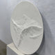 Selene V White Sandstone Textured 3D Wood Relief Wall Art, oval shape with eroded cliff-like texture, leaning against a light grey wall on a stone platform.