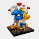 The Smurf Couple Kissing Love Sculpture - 60cm by Giant Sculptures features two Smurfs kissing on a black base with gold-detailed shoes and hair, topped with three red hearts—a vibrant pop art piece full of love and charm.
