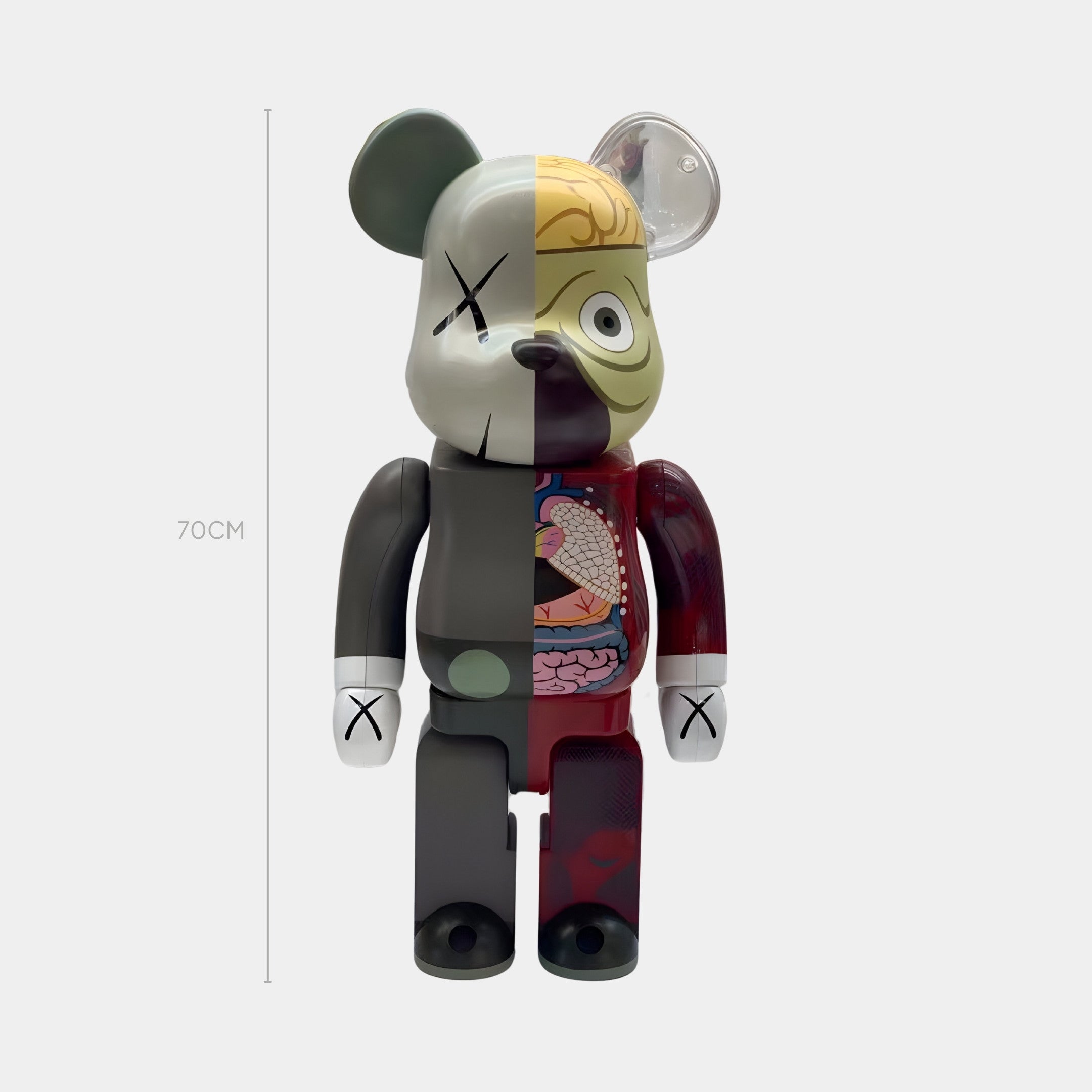 The Split Anatomy Rouge Bear Sculpture - 70cm by Giant Sculptures features a whimsical bear split in half—one side solid with muted colors, the other side exposing anatomical details like brain and heart. It sports Xs for eyes and a neo-medical cartoon art style.
