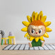 The Flower Elves Sunflower Labubu Sculpture - 160cm by Giant Sculptures, with hand-painted petals, orange hair, and big eyes, sits on a checkered rug in a modern minimal living room with small chairs and a decorative flower.