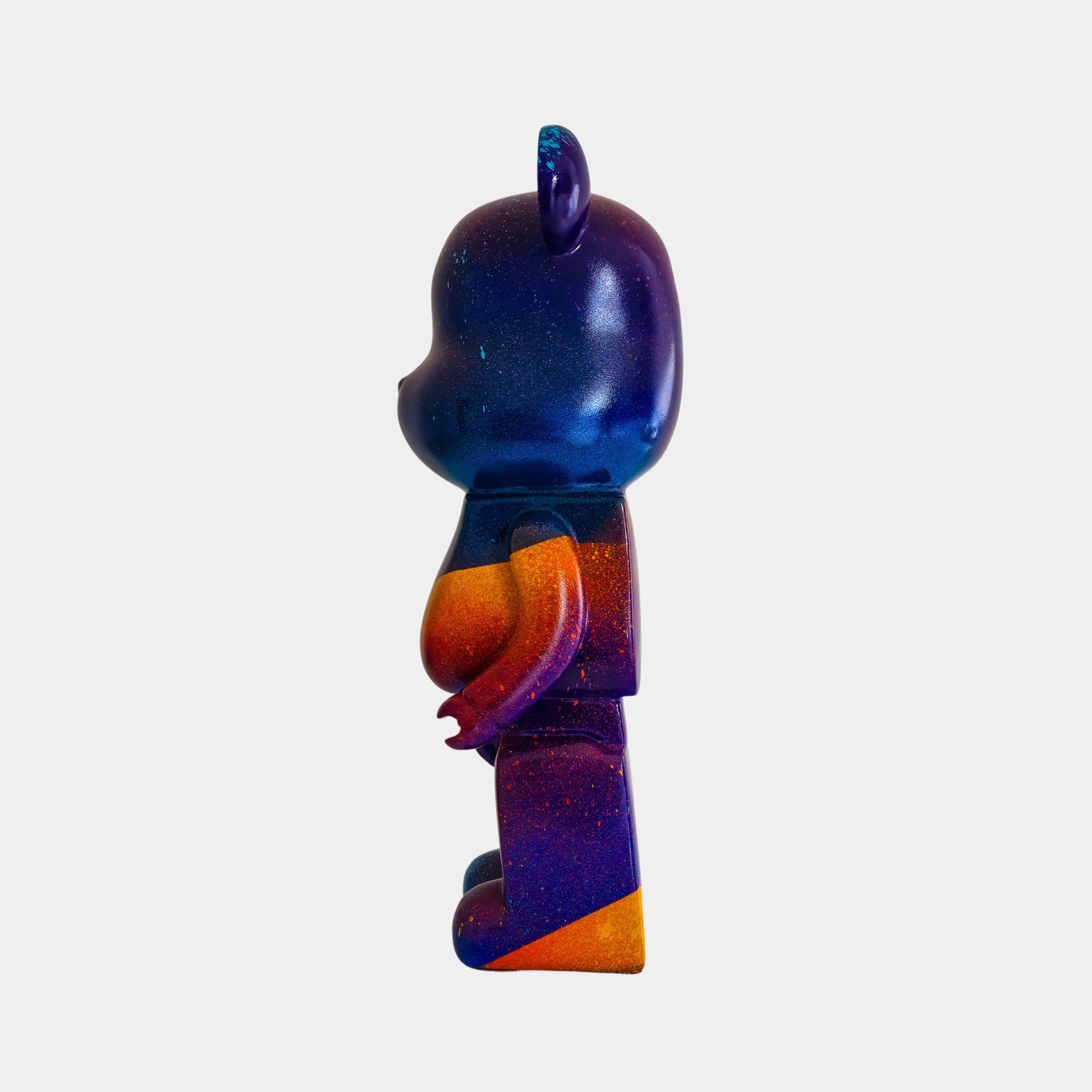 Side view of the 50cm Midnight Sunset Bear Sculpture by Giant Sculptures, featuring a vibrant bear-shaped design with blue, purple, orange, and red gradient hues. The glossy figure is displayed against a plain white background.