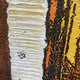 Close-up of the Terralume Amber Rust Abstract Textured Framed Wall Art showing a raised beige vertical stripe amid dripped orange, yellow, and rust-brown textured paint.