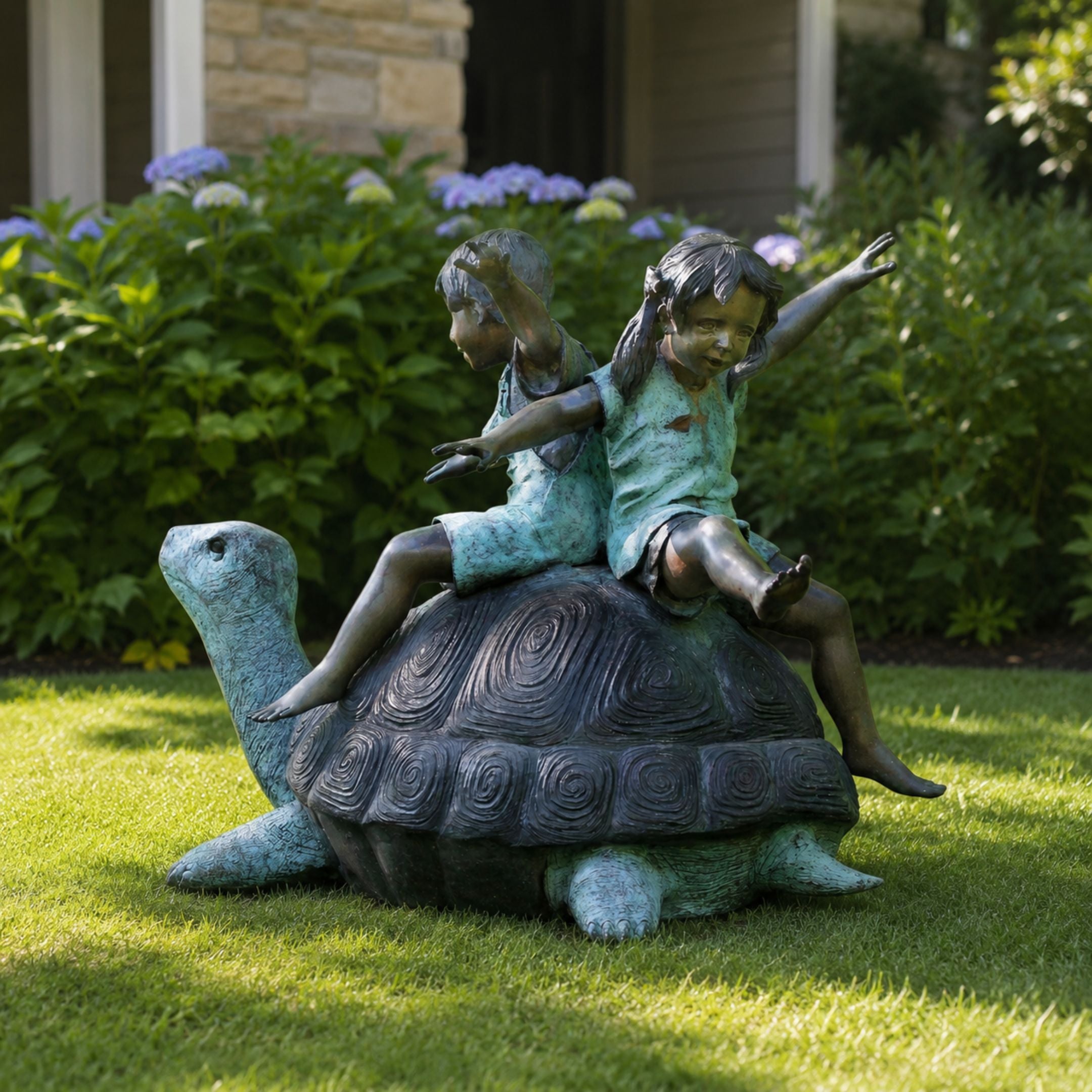 Traditional Children on Tortoise Bronze Sculpture, 140cm, shown outdoors on grass with two children raising their arms atop a spiral-shelled tortoise, set against green shrubs and purple flowers.