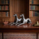 Traditional Reclining Greyhound Pair Bronze Sculpture by Giant Sculptures displayed on a polished wooden desk in a library with book-lined shelves.