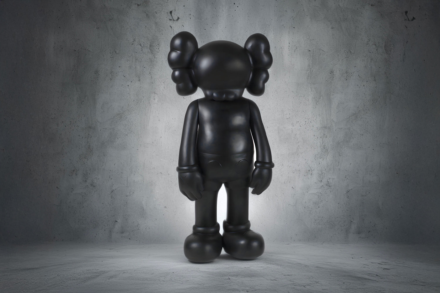 A standing, matte black sculpture in a cartoonish humanoid shape, positioned against a textured gray background. The figure is characterized by its rounded limbs and simplistic facial features, offering a contemporary, abstract aesthetic.