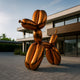 The 200 cm Sunset Orange Balloon Dog Sculpture by Giant Sculptures stands on a paved area before a modern building, its shiny surface reflecting the surroundings. The clear sky enhances the minimalist design and large windows of the structure.