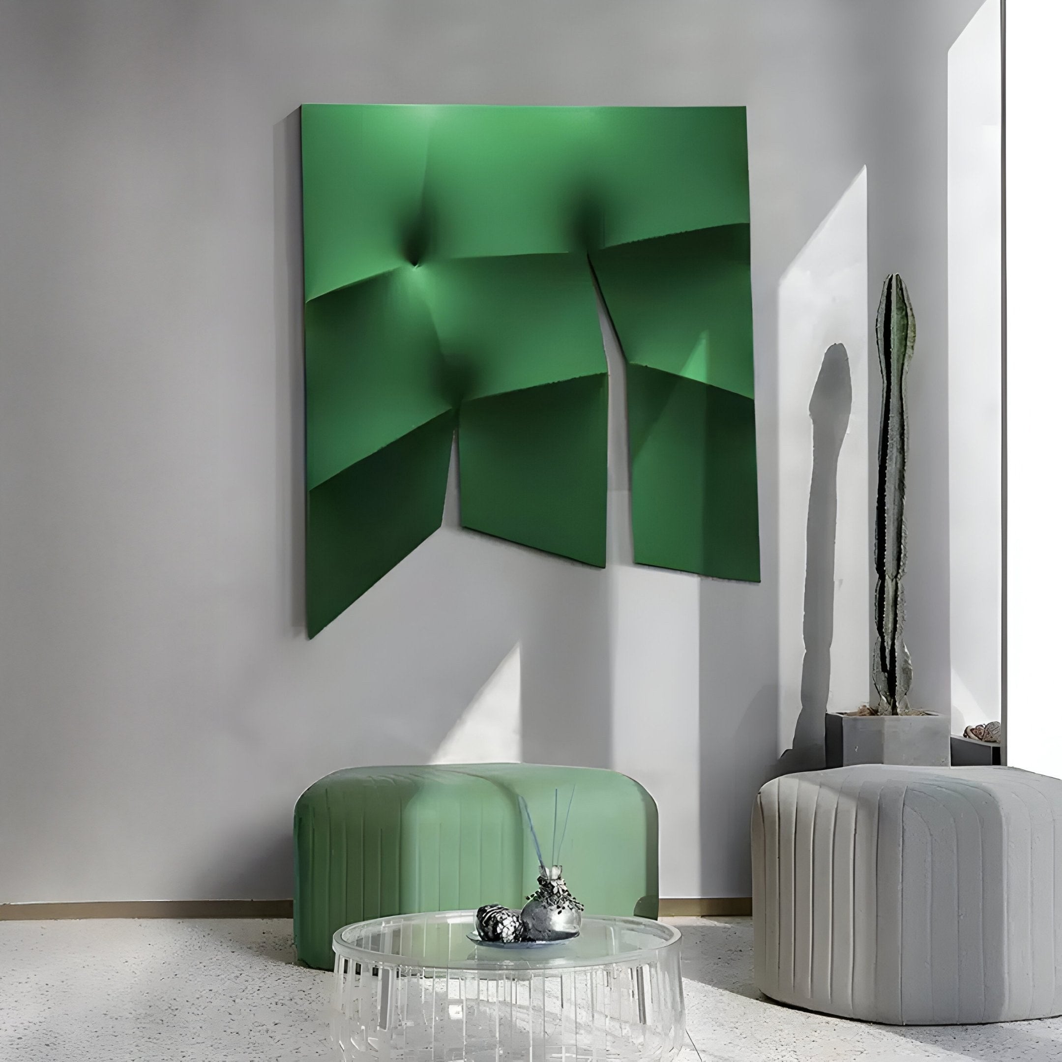 A modern interior features the Contours Emerald Green Elastic Fabric 3D Wooden Wall Art by Giant Sculptures, paired with two round ottomans—one green and one gray—and a glass coffee table with silver decor. A tall cactus by a sunlit window casts shadows on the white walls and floor.