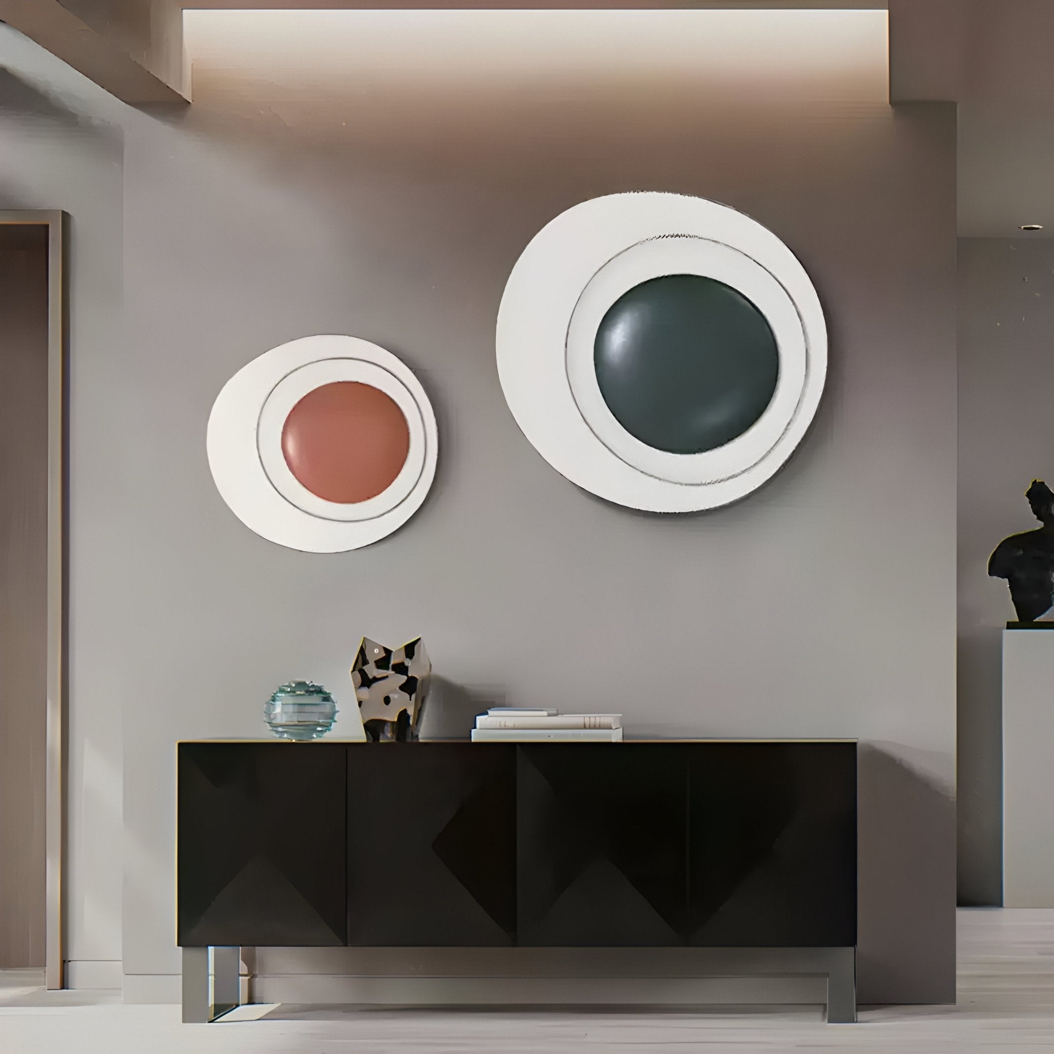 A modern living room features a black sideboard with decor like a small sculpture and glass orb, while above hang two Aetherial Green Glossy Circular Asymmetry 3D Wall Art pieces by Giant Sculptures, with white, black, and red concentric designs in asymmetrical frames.