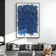 A modern living room includes a gray sectional sofa and a large abstract artwork featuring blue, cursive shapes on white. Its accented with a round white lamp, dried plants in a vase, and the Oratoria Blue Scripted Wood Carving Hand-Painted 3D Wall Art by Giant Sculptures for added depth.