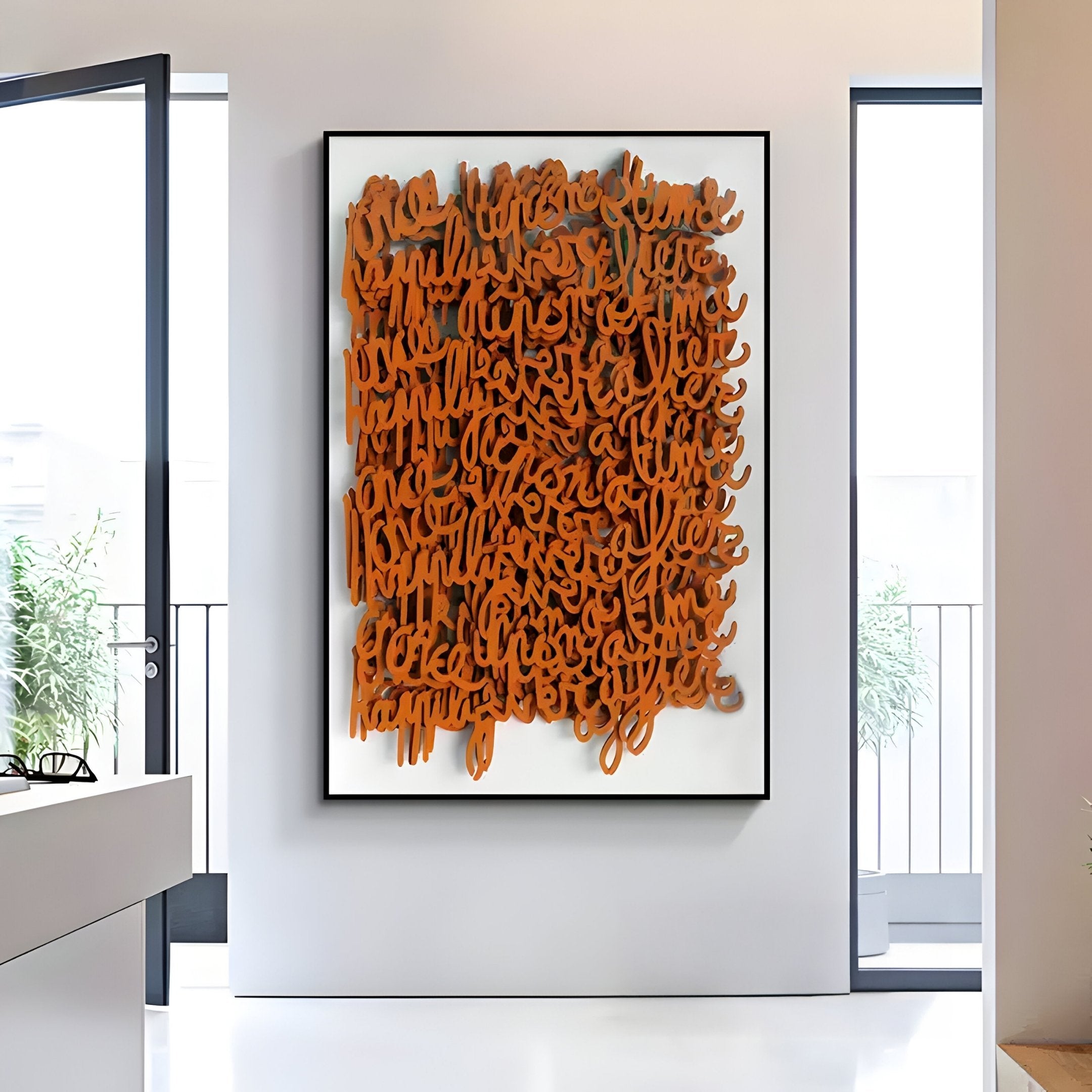 The Oratoria Orange Scripted Wood Carving Hand-Painted 3D Wall Art by Giant Sculptures is showcased in a well-lit room with large windows and minimal decor. A potted plant seen through the window adds to the airy, contemporary ambiance.