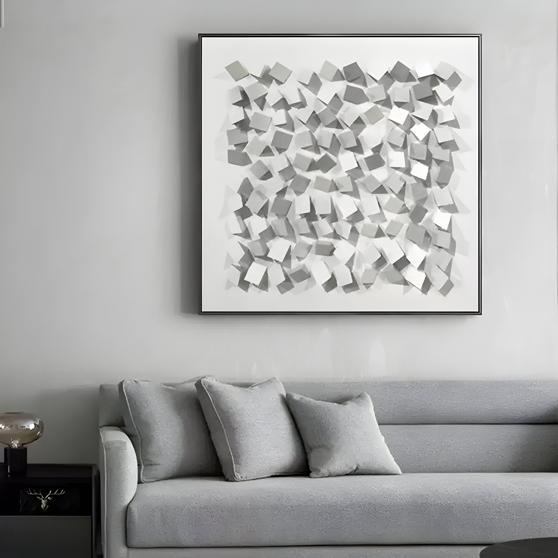 A modern living room showcases a light gray sofa with two matching cushions. Above, the Cubitara White Abstract Wood Cluster 3D Wall Art by Giant Sculptures, featuring numerous small geometric squares, adds a stylish touch to the plain wall.