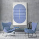 Two modern blue chairs face each other in front of an Ellipse Lavender Oval Wood 3D Canvas Wall Art by Giant Sculptures on a gray textured wall. A glass coffee table with decorative wire sculptures complements the serene ambiance of the white wooden floor between the chairs.