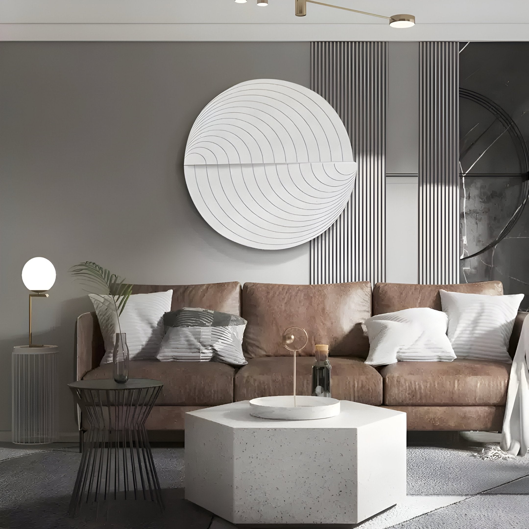 A modern living room features a brown couch with white pillows, Giant Sculptures Orbitals White Circular Wood Carved Sandstone 3D Wall Art, a round lamp on a tall side table, a vase on the glass coffee table, and a hexagonal white table against the gray and white paneled wall.