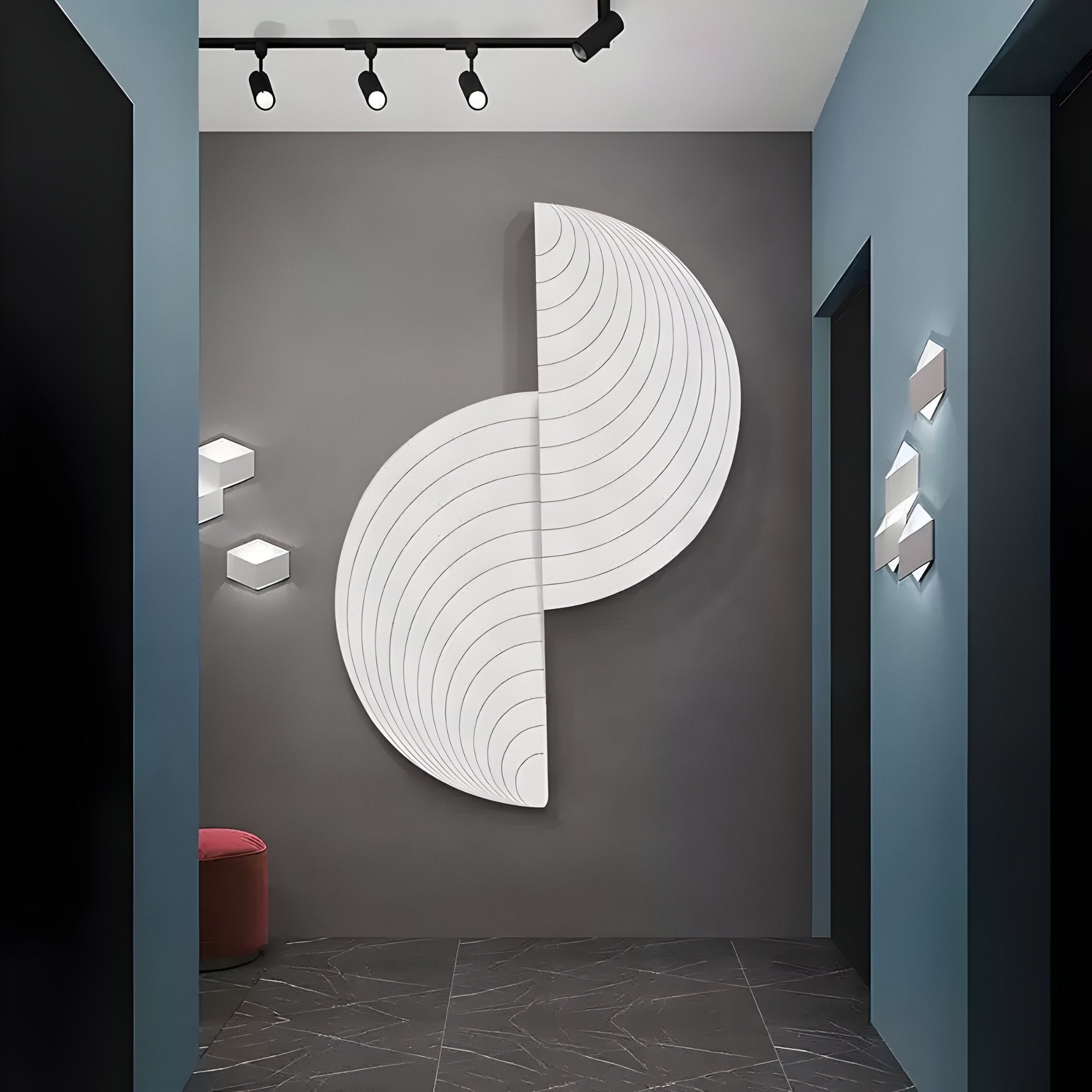 A modern hallway features the Orbitals White Semi-Circle Wood Carved Sandstone 3D Wall Art by Giant Sculptures, illuminated by black track lights. Blue and gray walls complement a red cushioned seat in the corner, while a subtly patterned dark floor completes the minimalist look.