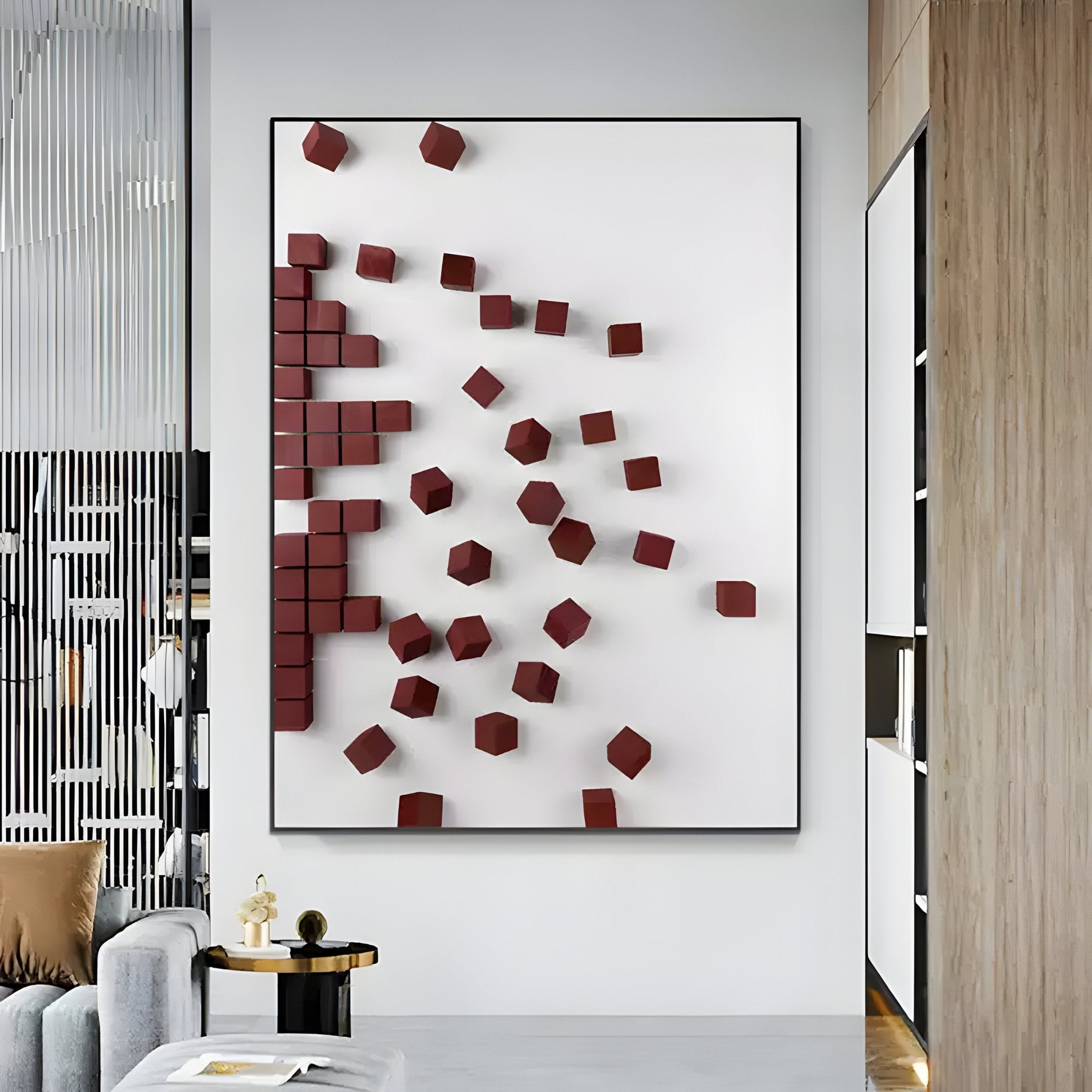 A modern living room features contemporary interiors with the Fragmenta Red Wooden Cube Scatter On White Canvas 3D Wall Art by Giant Sculptures. To the left, a gray sofa with a brown cushion sits next to a sleek black side table holding a book, and vertical black slats divide the space.