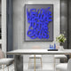 A modern dining area includes a white table and chairs adorned with a vase of white flowers and two blue bottles. Adding flair to the contemporary interiors is the Giant Sculptures Urbanic Blue Welcome Script 3D Wooden Graffiti Wall Art, which reads Welcome to the Circus.