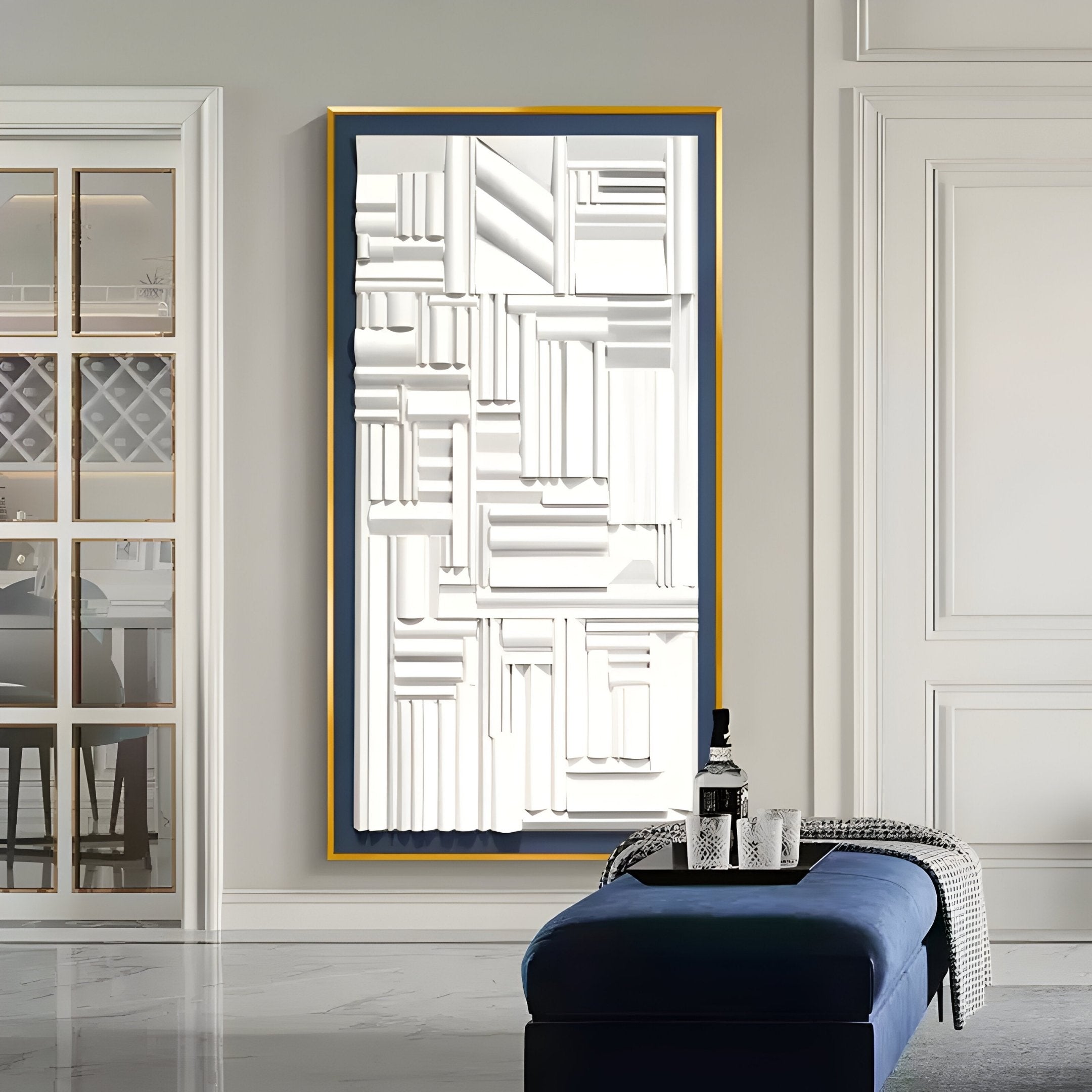 A modern interior showcases the Forma Blue-Frame White Geometric 3D Wooden Vertical Wall Art by Giant Sculptures. Below it is a plush blue bench with a patterned throw and a bottle. The room features elegant wall paneling, an aluminum alloy frame, and a reflective glass door.