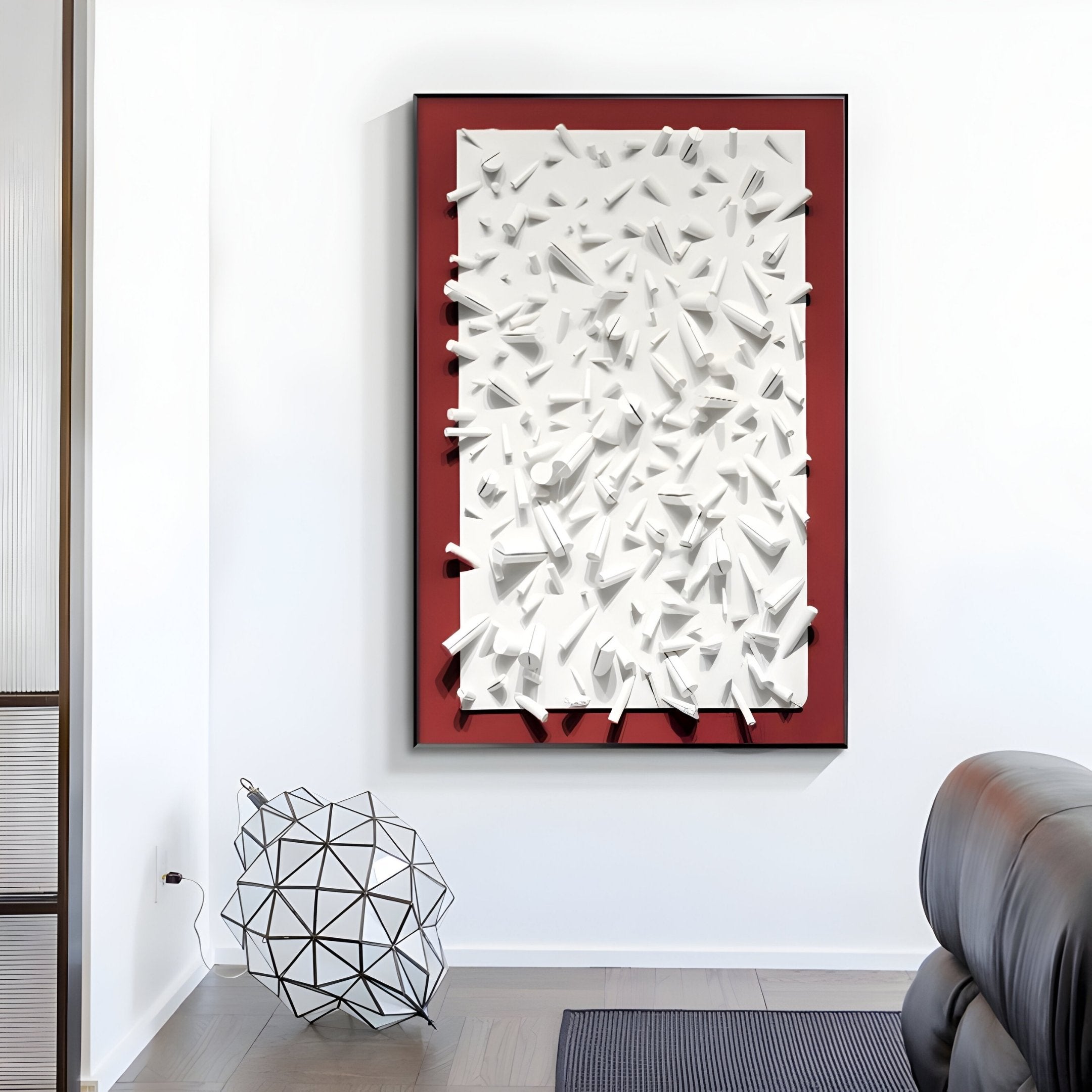 Displayed in a gallery, the Artiora Red Edge & White Abstract Wooden Shard 3D Wall Art by Giant Sculptures features a 3D white abstract design on red and is complemented by geometric sculptures and wooden shards. A leather sofa is partially visible to the right, enhancing the modern setting.