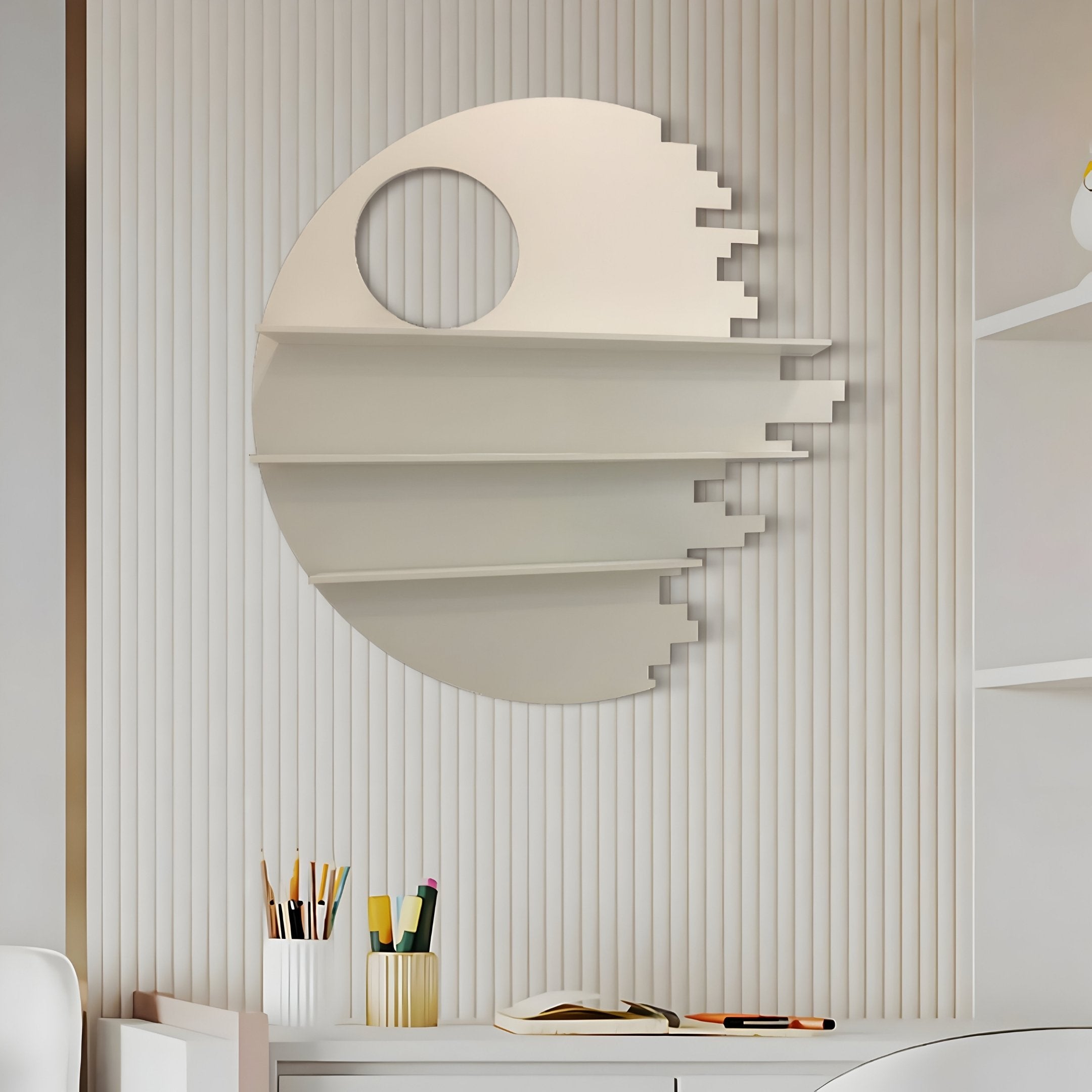 An Orbis White Geometric Multi-Tier Decorative Shelf by Giant Sculptures, reminiscent of a sci-fi space station, adorns the ribbed wall. Below it, a desk holds pencils, pens, a notebook, and an eraser. The room features minimalist modern design elements for a sleek contemporary look.