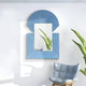 The Aurellis Blue Arch & Square Geometric Mirror Frame by Giant Sculptures reflects a tall green plant, while a light blue cushioned chair with a wooden base complements the white wall, creating a minimalist and fresh interior vibe.