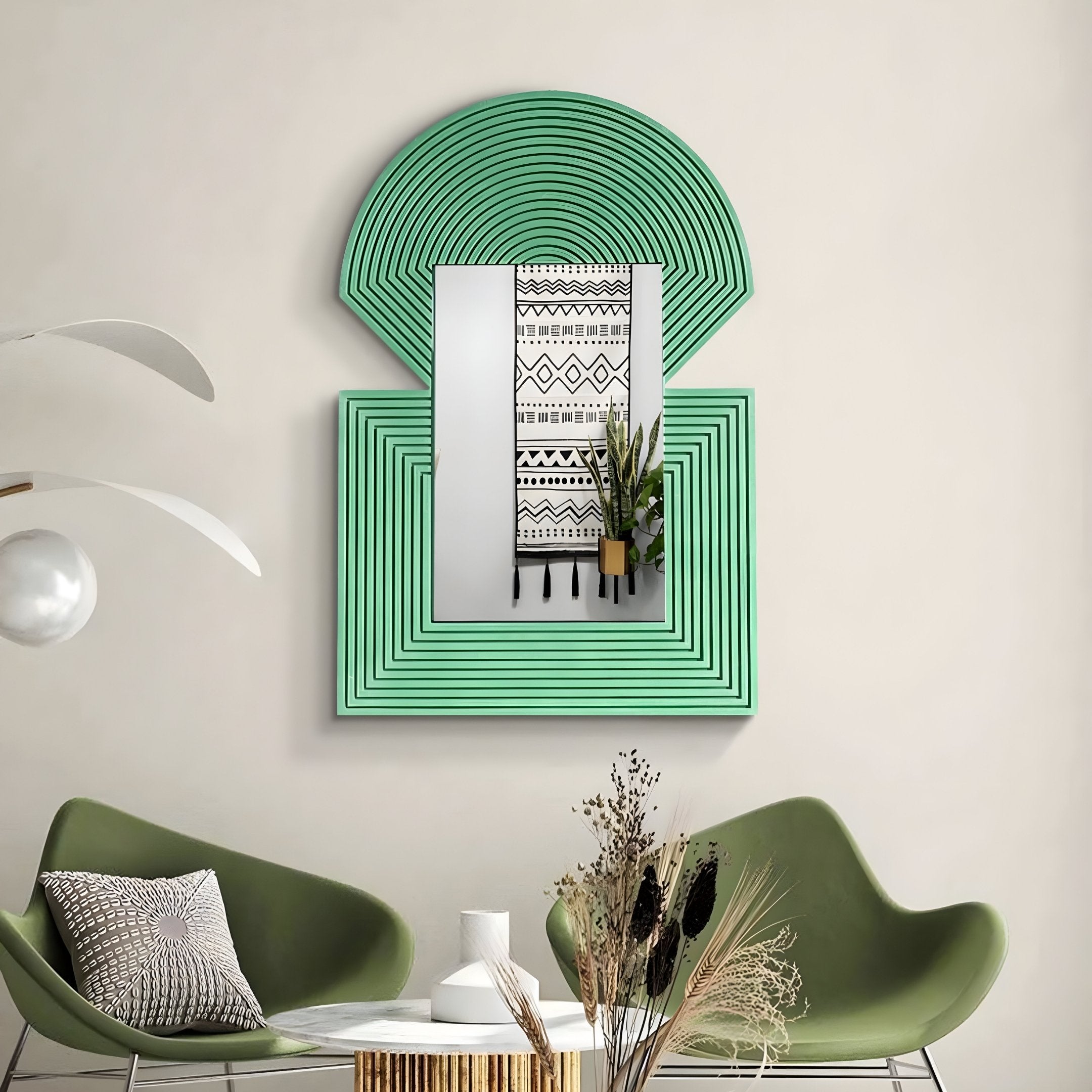 A modern interior features the Aurellis Green Arch & Square Geometric Mirror Frame Wall Art by Giant Sculptures and a black-and-white patterned hanging. Two green armchairs flank a small white table with dried flowers, accompanied by a decorative plant and a lamp with a spherical bulb.