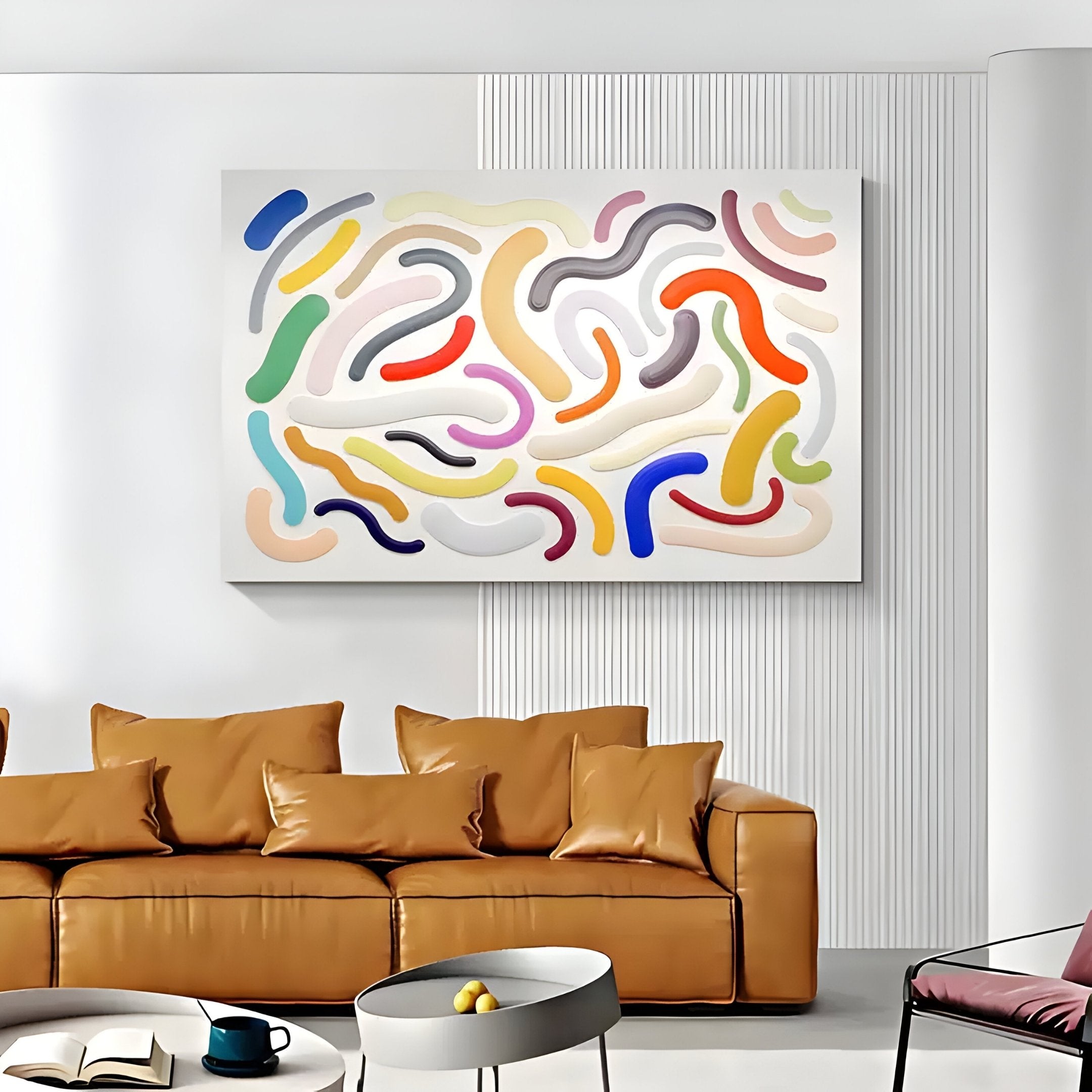 In a minimalist living room, a tan leather sofa is adorned with cushions, accompanied by a round gray coffee table holding a book and cup. Above hangs the Chromisma Multicolour Abstract Curves hand-painted 3D wall art by Giant Sculptures.