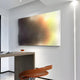 A modern, minimalist room showcases a sleek wooden desk with a brown leather chair and a glass of whiskey. On the white wall hangs the Wavluxe Gradient Sunset Glow Wood Mosaic 3D Wall Art by Giant Sculptures, enhancing this stylish interior with its abstract grid pattern and sunset radiance.