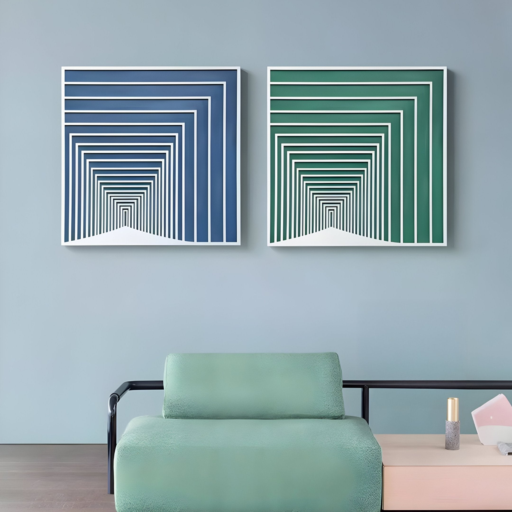 A modern living room showcases a minimalist green sofa alongside two Prismalux Blue Wood Carving Hand-Painted 3D Wall Art pieces by Giant Sculptures, featuring blue gradient concentric squares for a tunnel illusion. A small side table with a candle and notebook completes the scene.