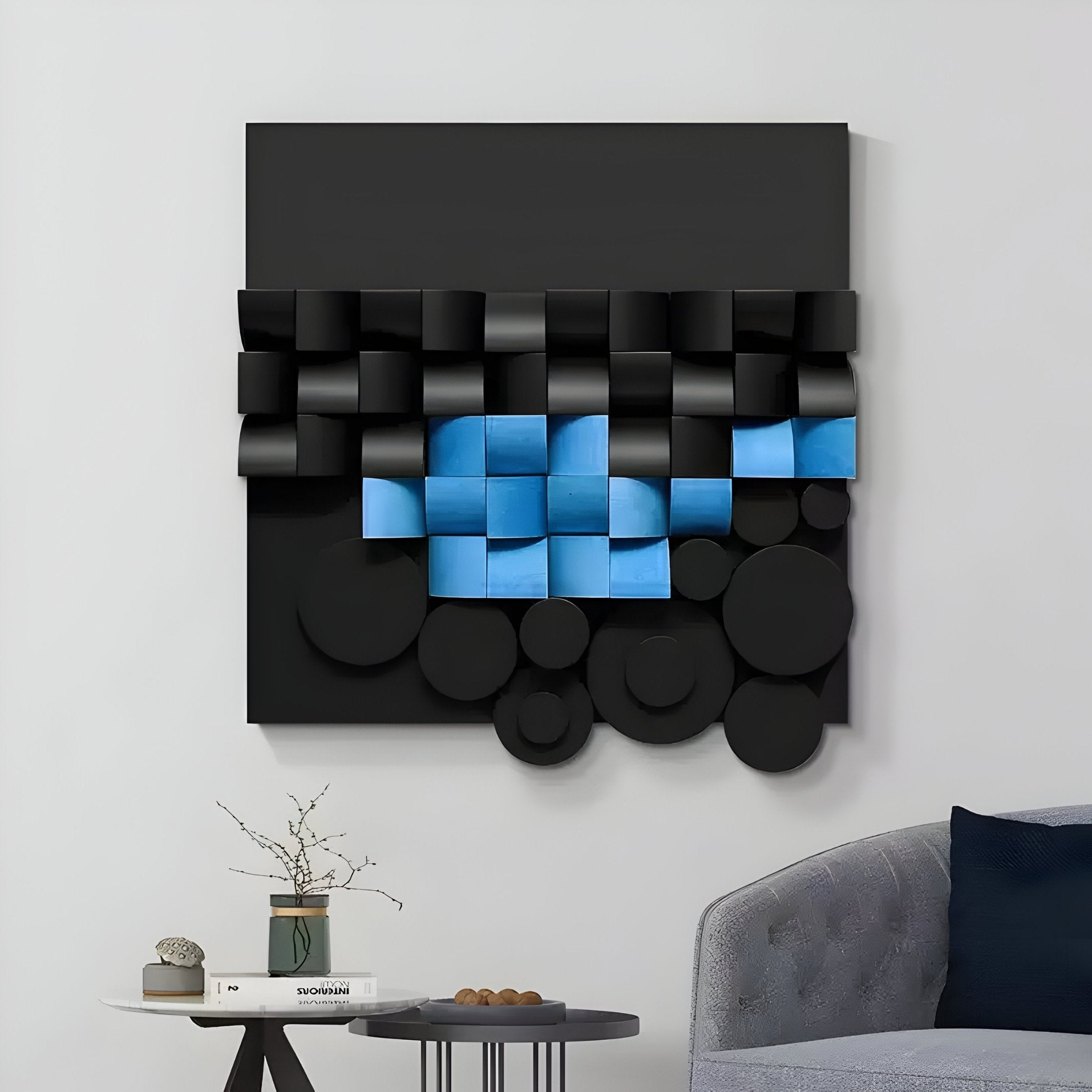 The Nocturna Black & Blue Modular Wooden Hand-Painted 3D Wall Art by Giant Sculptures features overlapping geometric shapes in a grid with circular and square elements for depth. A small white table with a vase beside a gray cushioned chair complements this contemporary piece.